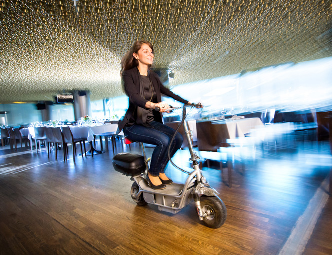 Tugba Coskun fährt mit einem kleinen Elektroroller durch einen Veranstaltungsraum.