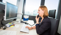 Bürokommunikationskauffrau Laura Kohlhöfer telefoniert von ihrem Schreibtisch aus und betrachtet dabei ein Dokument auf ihrem Computerbildschirm.